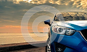 Blue compact SUV car with sport and modern design parked on concrete road by the sea at sunset in the evening. Hybrid and electric