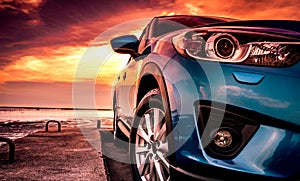 Blue compact SUV car with sport, modern, and luxury design parked on concrete road by the sea at sunset. Front view of beautiful