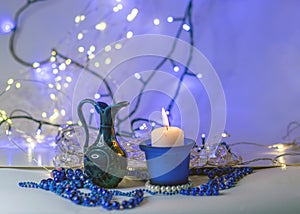 Blue composition with candle and miniature mug, blue pearl ornaments in the foreground, white and blue light chain background,