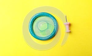 Blue condom and pin on yellow background