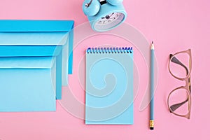 Blue correspondence envelopes, clock and notebook on pink background with copy space. Back to school or work concept