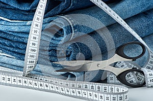 Blue cotton jeans are stacked on a table with a tape measure and scissors