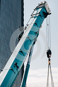 Blue crane lifting mechanism with hooks near the glass modern building, crane and hydraulic high lift up to 120 meters