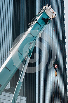 Blue crane lifting mechanism with hooks near the glass modern building, crane and hydraulic high lift up to 120 meters