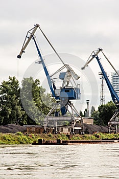 Blue cranes in cargo port translating coal, industrial scene