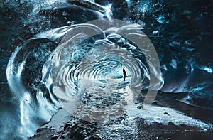 Blue crystal ice cave entrance with tourist climber and an underground river beneath the glacier located in the