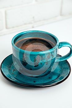 Blue cup of black coffee with a saucer on a white table. Front view