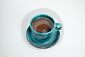 Blue cup of black coffee with a saucer on a white table. Top view