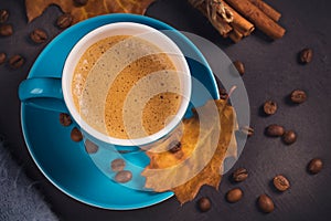 Blue cup of coffee with coffee beans and autumnal dry leaves