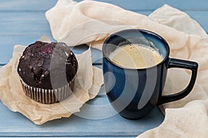 blue cup of coffee and chocolate muffin on wooden table