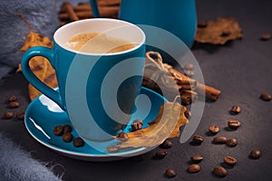 Blue cup of coffee with coffee beans and autumnal dry leaves