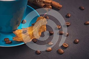 Blue cup of coffee with coffee beans and autumnal dry leaves