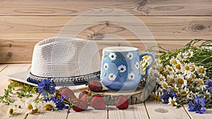 A blue cup of coffee with daisies, a bouquet of daisies and cornflowers, strawberries, a hat from the sun. Summer still life