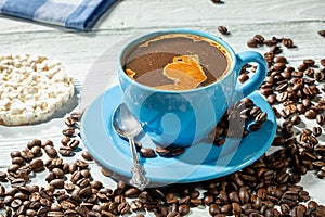 Blue cup of coffee with foam on a wooden table surrounded by scattered coffee beans