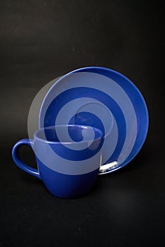 Blue cup of coffee and saucer on a black background.