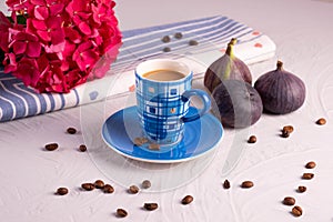 Blue cup of coffee, scattered coffee beans, 3 figs and a hydrangea branch