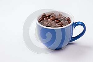 Blue cup full of coffee beans isolated on white.