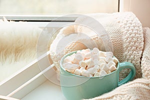 Blue cup of hot chocolate with marshmallow on windowsill with furskin for relax. Weekend concept. Home style.