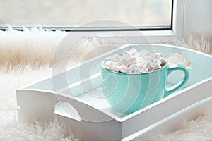Blue cup of hot chocolate with marshmallow on windowsill with furskin for relax. Weekend concept. Home style.