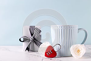 Blue cup with hot drink, white tender roses flowers, red lock in form of heart and box with gift