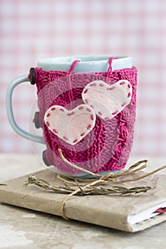 Blue cup in pink sweater with hearts standing on notebook