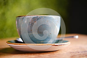 Blue cup, saucer and spoon on a wooden table of a summer cafe, close up