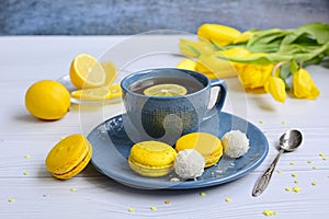 Blue cup of tea with lemon, yellow macarons, coconut cookies and tulips on a light background. Home relax