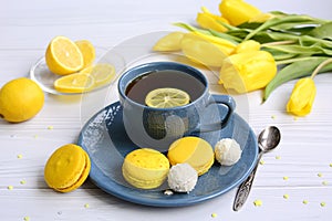 Blue cup of tea with lemon, yellow macarons and tulips on a light background