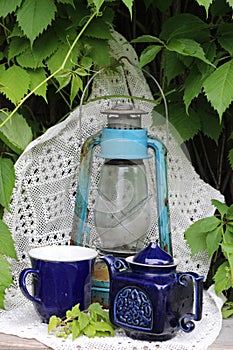 Blue cup and teapot stand on a white tablecloth against the background of a vintage lantern