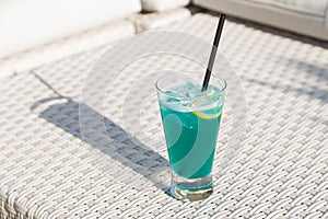 Blue Curacao Beach Cocktail with fresh lemon standing on a landing stage, with palm in background