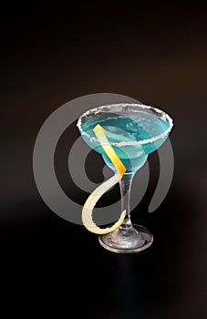 Blue curacao, beach cocktail with ice and lemon zest on a black background