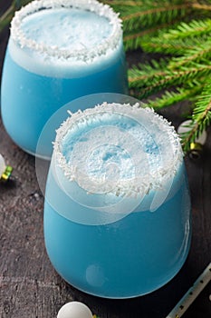 Blue curacao Christmas Cocktail, garnished with coconut on Christmas decorated holiday table with Christmas ornaments. Holiday