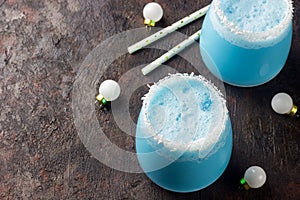 Blue curacao Christmas Cocktail, garnished with coconut on Christmas decorated holiday table with Christmas ornaments. Holiday