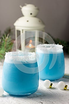 Blue curacao Christmas Cocktail, garnished with coconut on Christmas decorated holiday table with Christmas ornaments. Holiday