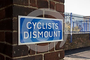 Blue Cyclists Dismount sign on brick wall outside