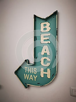 A blue decorative post sign beach this way hanging on the white wall