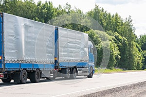 Blue delivery van and white truck driving on the asphalt road between line of trees in autumn landscape