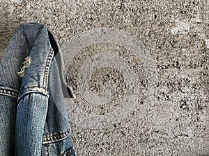 Blue denim jacket hang on nail hammer in rough cement wall. Wrinkle pattern concrete texture background.