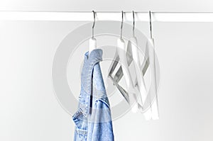 Blue denim jacket on white wooden coat hanger on a rod against light gray wall flat lay copy space. Denim, fashionable jacket,