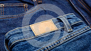 Blue denim jeans with emty label. Brown blank leather label tag on denim pants background. Blank mockup beige leather