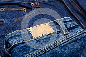 Blue denim jeans with emty label. Brown blank leather label tag on denim pants background. Blank mockup beige leather