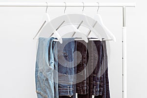 Blue denim jeans hanging on white clothes hangers on portable clothing rack.