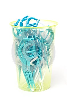 Blue dental floss sticks in plastic cup on a white background