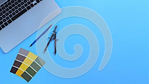Blue desktop with architect designer tools consisting of paint sample cards and laptop