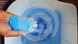 Blue detergent powder in hands and adding it in water in washing machine