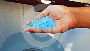 Blue detergent powder in hands and adding it in water in washing machine