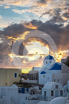 A blue dome church in Oia village, Santorini island, Greece during sunset. Sun rays shining through the clouds