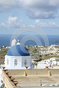 The blue-domed church in Santorini surrounded by buildings and the sea at daytime in Greece