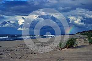 Blue dramatic clouds and rainbow over the beach