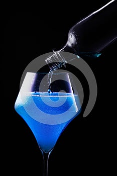 Blue drink is poured into a glass. Black background